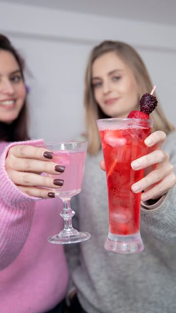 Deux invitées trinquent avec des cocktails préparés par Eterna Event : un cocktail rosé dans un verre à pied et un cocktail rouge glacé garni d'une brochette de fruits rouges